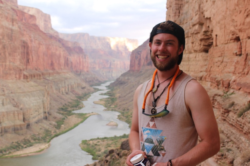 Max smiling on a ledge high above the Colorado River, the Grand Canyon stretching into the distance behind him.